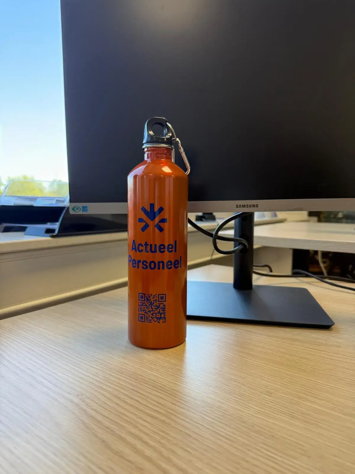 Oranje drinkfles van Actueel Personeel met QR-code op een bureau