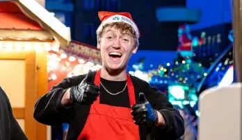Lachende man met kerstmuts en rode schort die zijn duimen opsteekt