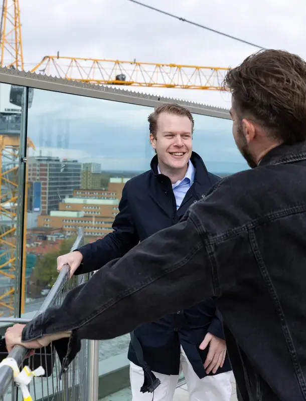 Twee mannen in gesprek op een bouwsteiger met uitzicht over de stad