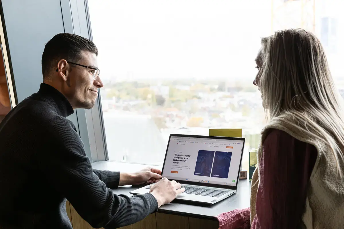 Twee mensen aan het werk achter een laptop bij het raam