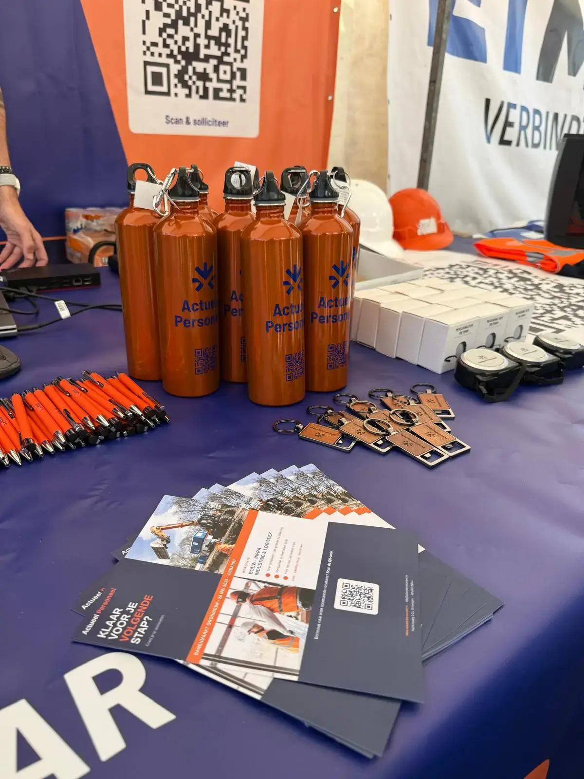 Oranje drinkflessen, pennen en folders op de tafel van onze stand